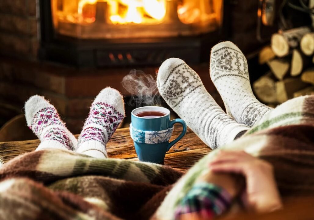 Cozy scene: two people relaxing by fireplace with steaming tea, warm atmosphere.