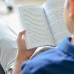Person reading book in cozy room with serene lighting, immersed in quiet concentration.