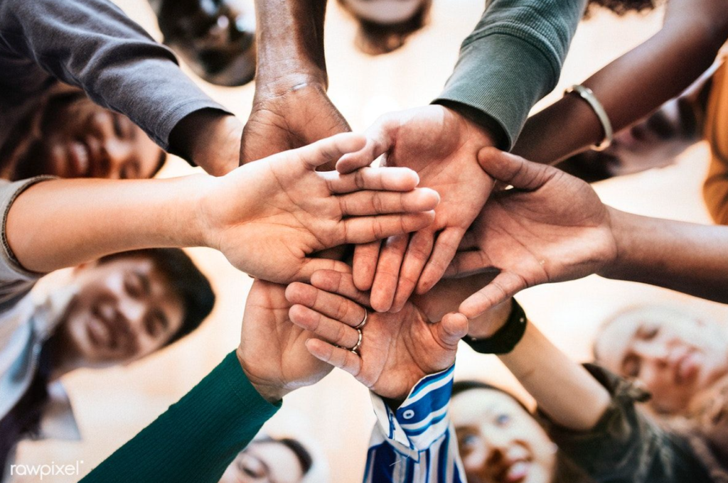 A group of diverse people stacking their hands together in a gesture of teamwork and unity, viewed from a low angle.