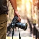 Photographer capturing golden hour light in forest with DSLR camera.