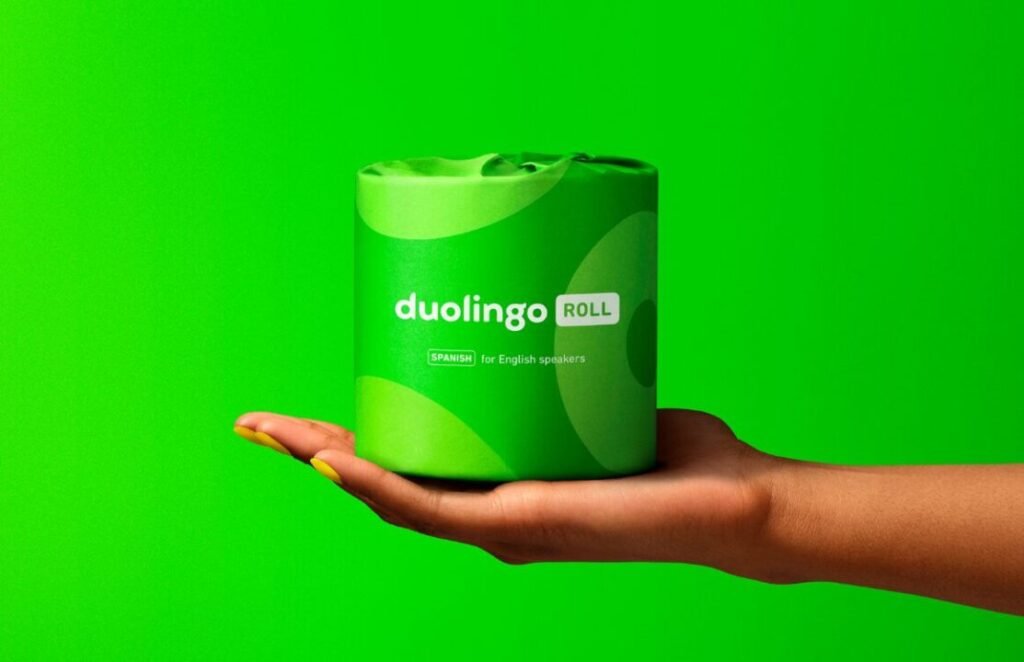 A hand holding a green cylindrical object labeled "Duolingo ROLL Spanish for English speakers" against a matching green background.