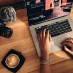 Modern workspace with laptop editing, camera, coffee, and tech gear for content creation.