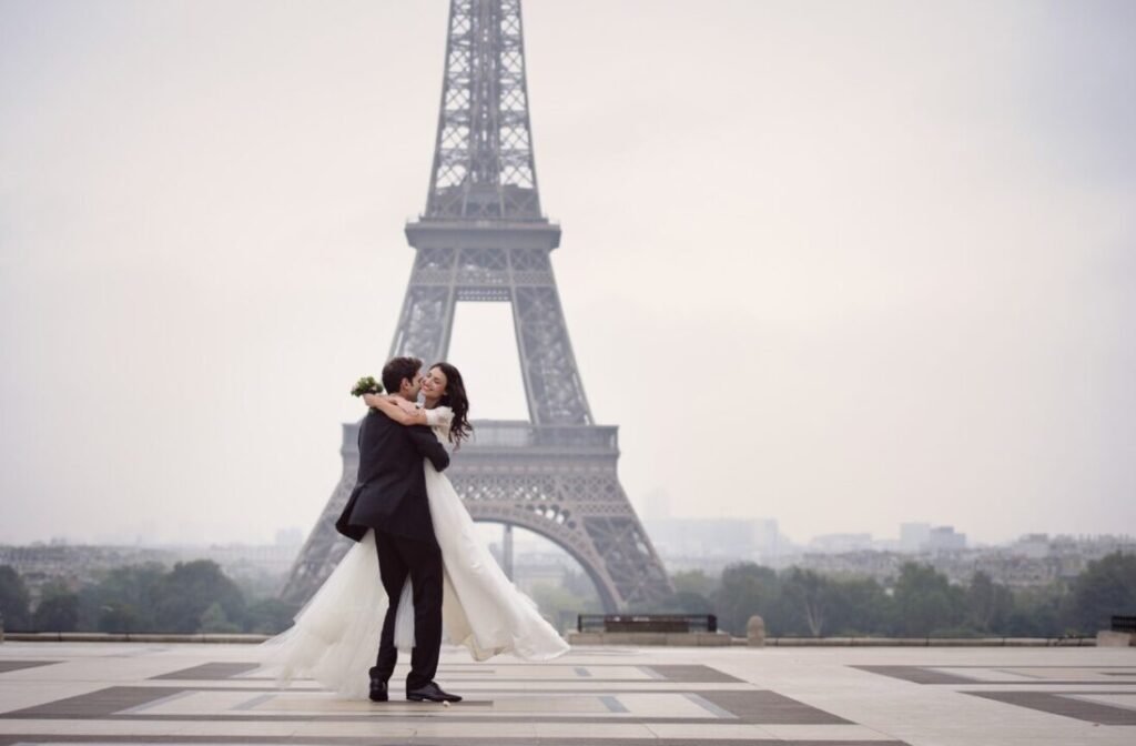 A bride and groom embracing in front of the Eiffel Tower on a hazy day.