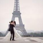 Romantic Eiffel Tower kiss: couple embraces in elegant attire for special occasion.