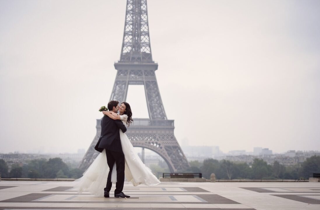 Romantic Eiffel Tower kiss: couple embraces in elegant attire for special occasion.