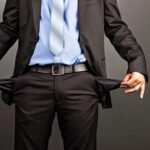 Man in formal suit showing empty pockets symbolizing financial distress or bankruptcy.