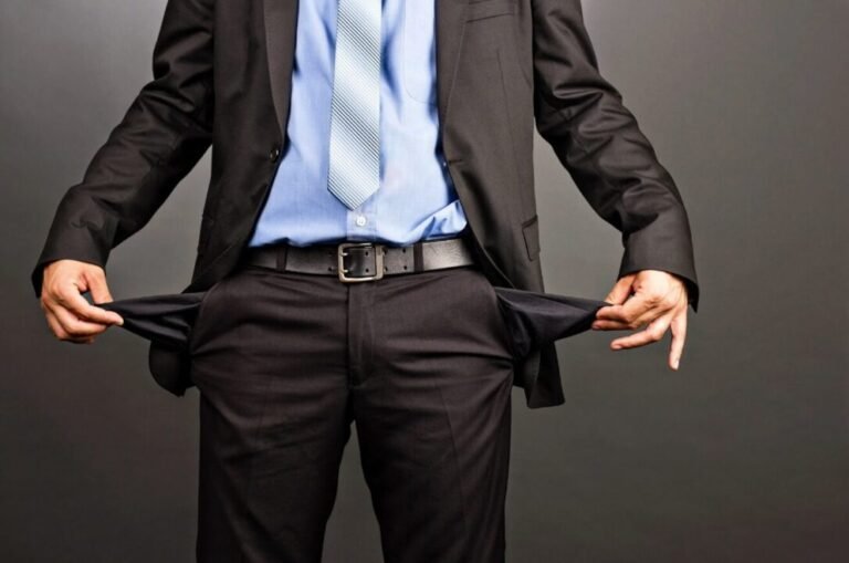 Man in formal suit showing empty pockets symbolizing financial distress or bankruptcy.