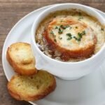 Delicious French Onion Soup with Melted Cheese, Herbs, and Toasted Baguette.