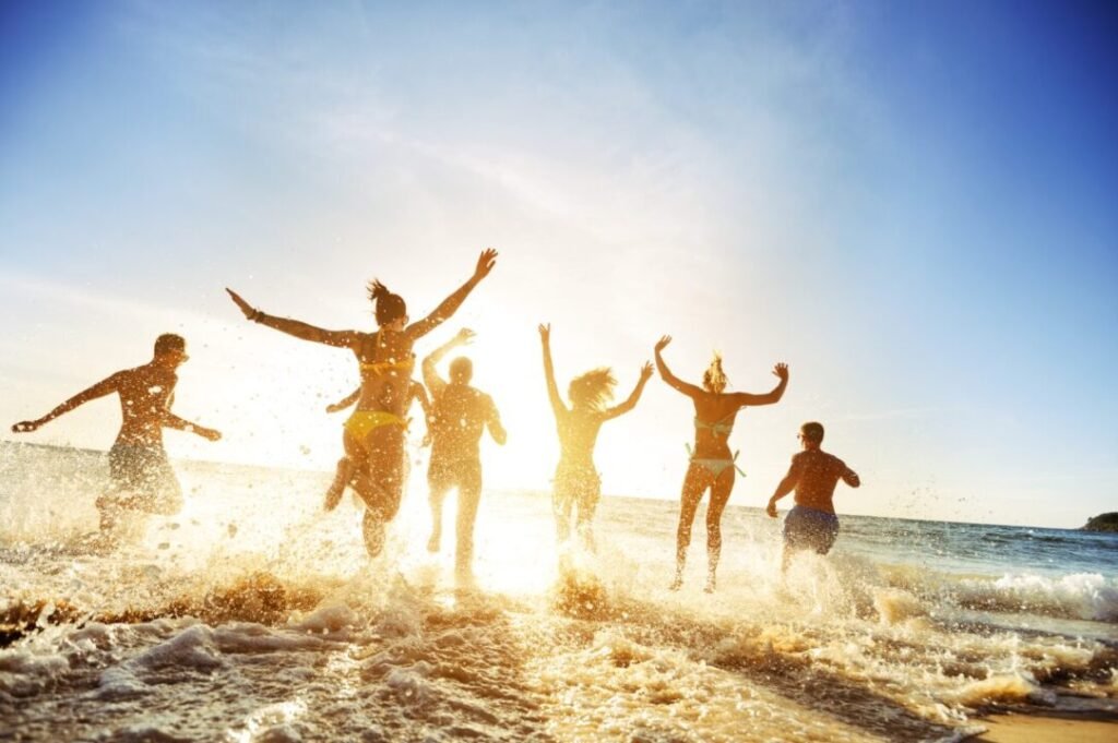 Group of young people joyfully jumping and splashing in the ocean at sunset.