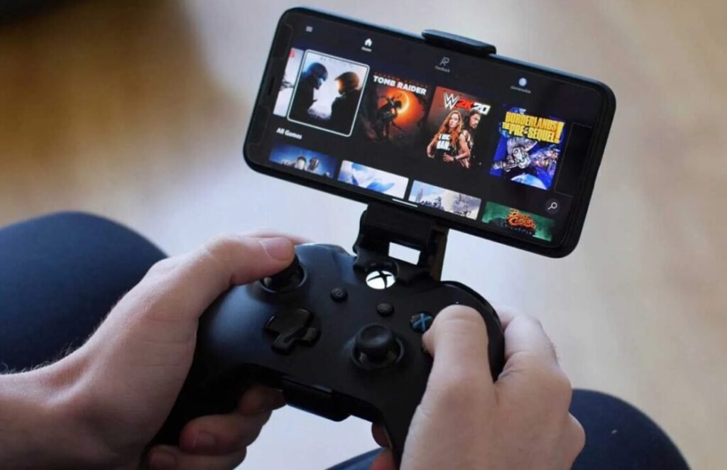 Hands holding an Xbox controller attached to a smartphone displaying a selection of video games.
