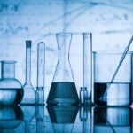 Glass laboratory equipment on reflective surface with scientific diagrams, showcasing precision and experimentation.