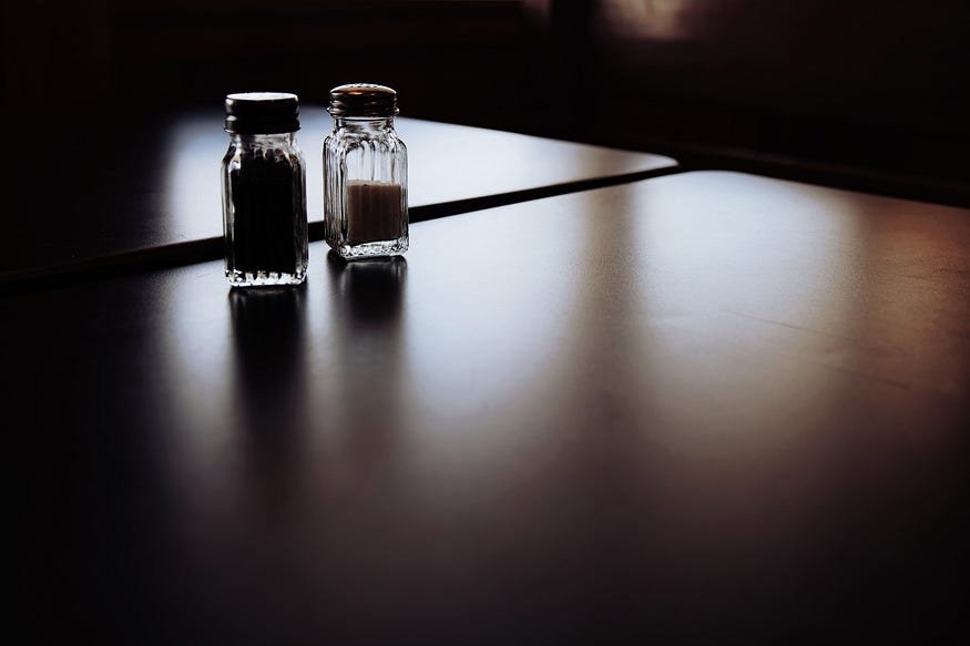 Glass salt and pepper shakers in dramatic lighting on dark tabletop.