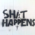 Urban graffiti art: SH*T HAPPENS with stick figures on white corrugated surface.