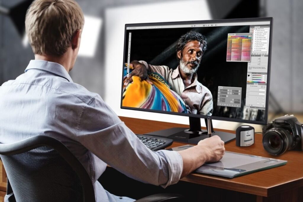 A person working on a graphic design project on a computer; the monitor displays an image editing application open with a close-up photo of a man holding colorful fabrics.