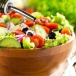 Fresh Greek salad with colorful veggies and dressing pour, ready to eat.