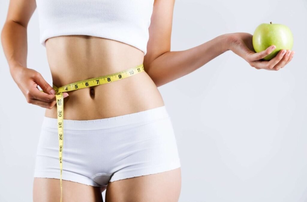 Woman holding a green apple in her right hand and a measuring tape around her waist, suggesting a concept of health and fitness.