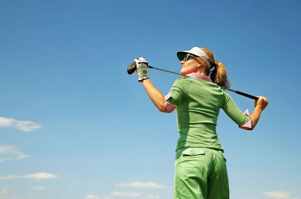 Woman in green golf attire swinging a club against a clear blue sky.