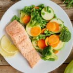 Fresh grilled salmon with vibrant veggies, lemon garnish, on white plate.
