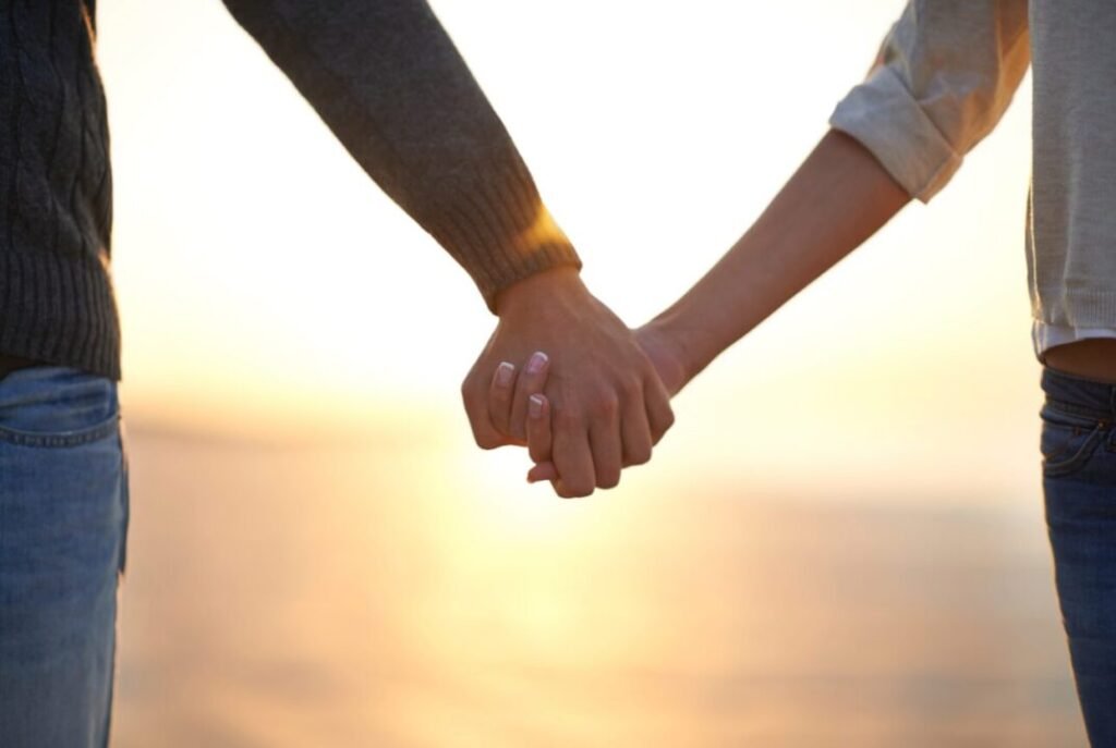 Close-up of two people holding hands with a sunset background.