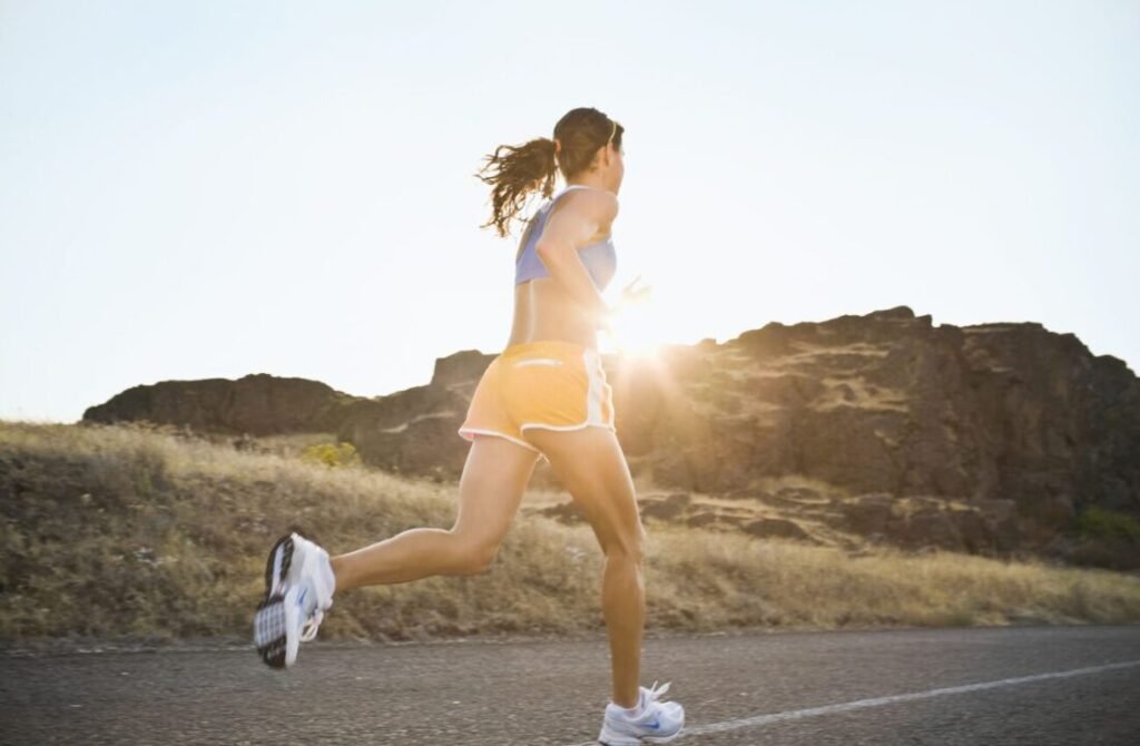 Woman running on sunlit road in rocky landscape, embodying determination and strength.