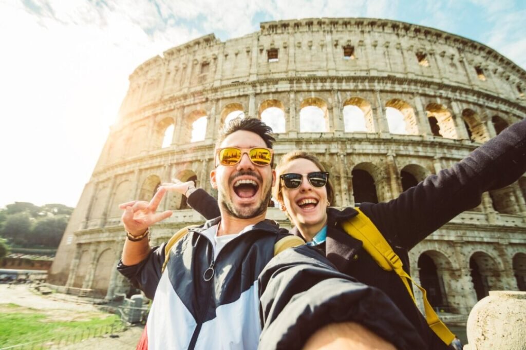 Two joyful tourists taking a selfie in front of the Colosseum in Rome, smiling and making playful gestures.