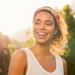 Young woman beaming with joy in sunlit nature, radiating happiness and warmth.