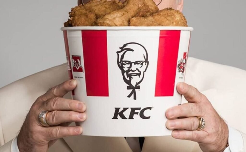 Man in white suit holding a large KFC bucket filled with fried chicken.