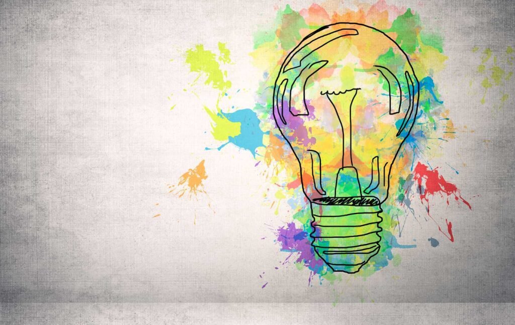 Vibrant light bulb surrounded by colorful watercolor splashes on textured gray background.