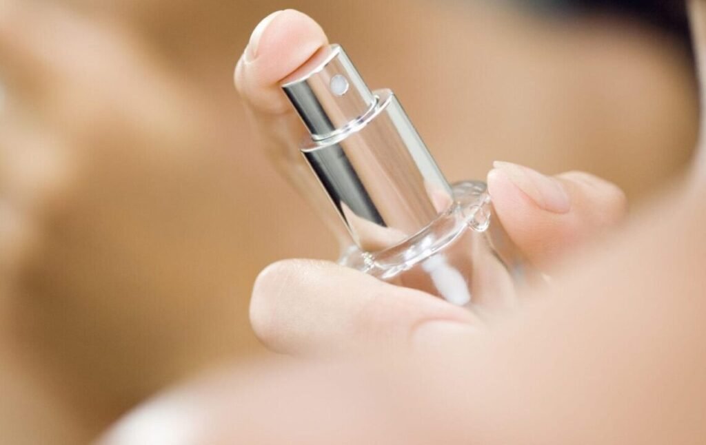 Close-up of a person holding a clear glass perfume bottle with a metallic cap.