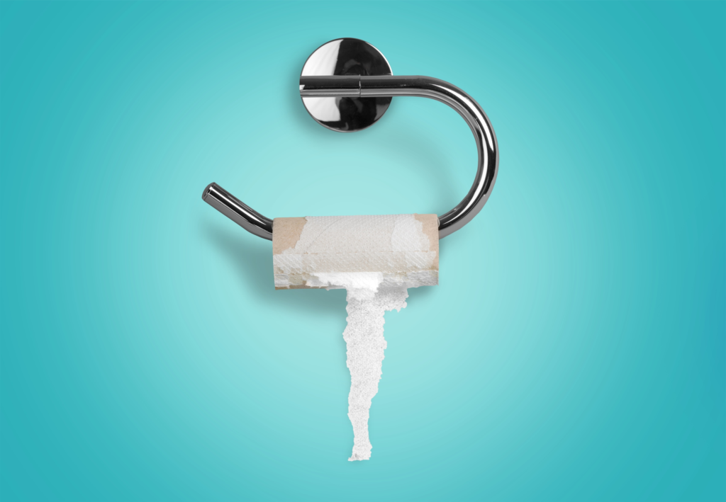 A chrome toilet paper holder mounted to a wall with an almost empty roll of toilet paper, with a single sheet hanging down, against a teal blue background.