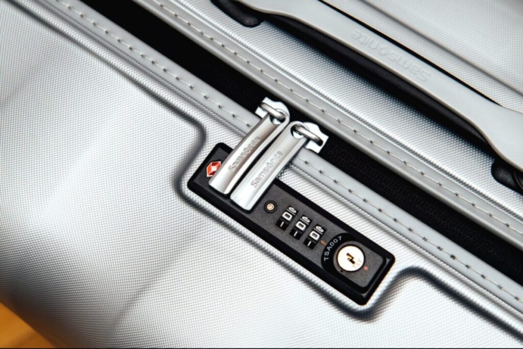 Close-up of a TSA-approved luggage lock on a silver suitcase, displaying a combination dial and keyhole.