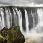 Majestic waterfall cascade with mist, cliffs, and dramatic clouds.