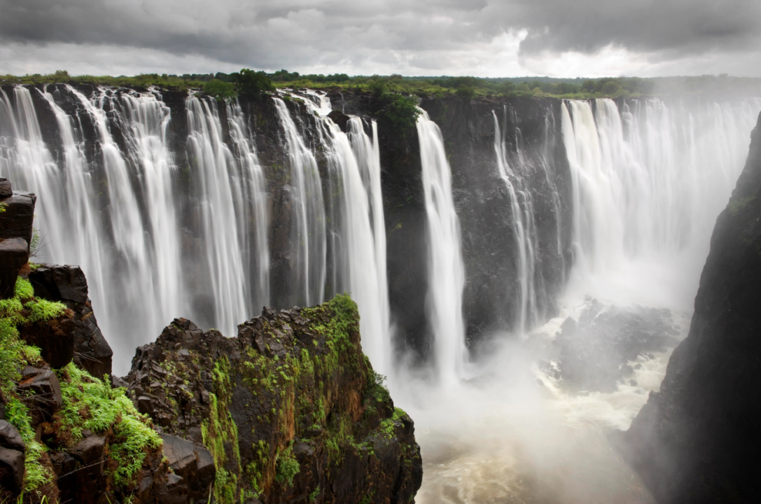 Majestic waterfall cascade with mist, cliffs, and dramatic clouds.