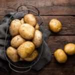 Golden-brown unpeeled potatoes in wire basket on dark wood surface, with rustic charm.