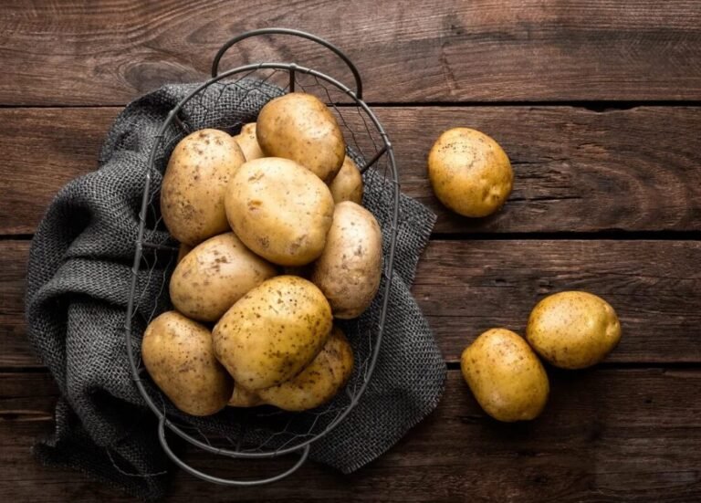 Golden-brown unpeeled potatoes in wire basket on dark wood surface, with rustic charm.