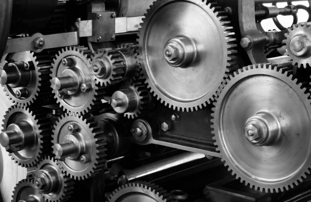 A black and white photograph of an interconnected set of various-sized metal gears and cogs in motion.