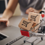 Mini shopping cart model on desk with laptop and mug symbolizing online shopping experience.