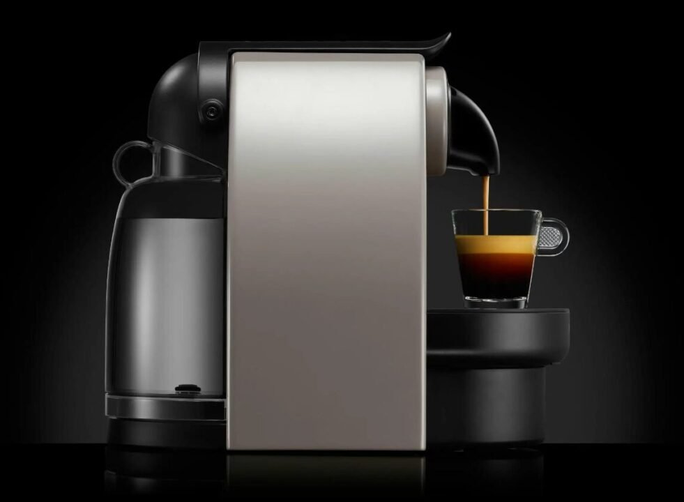 Modern espresso machine brewing rich espresso into glass cup on black background.
