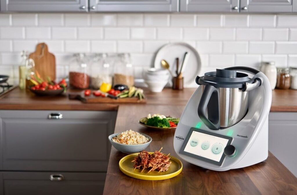 Modern kitchen with a multifunctional cooking appliance on the counter, surrounded by various dishes and ingredients.