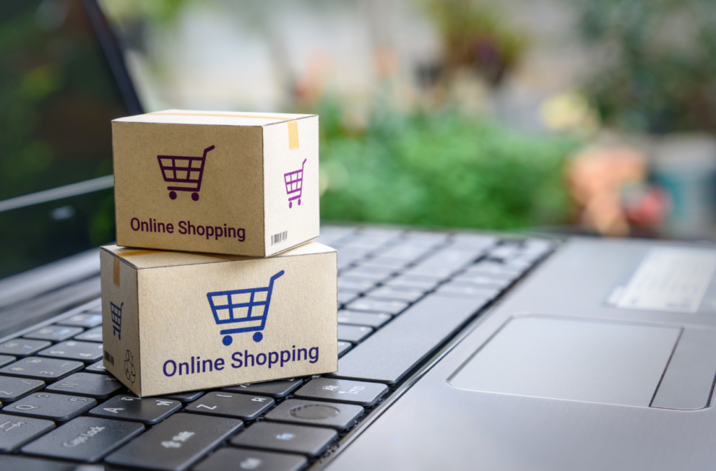 Two small cardboard boxes with "Online Shopping" and shopping cart icons printed on them situated on a laptop keyboard, with a blurred natural background.