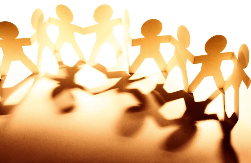 Golden paper dolls connected in a chain symbolize unity and community on an orange background.