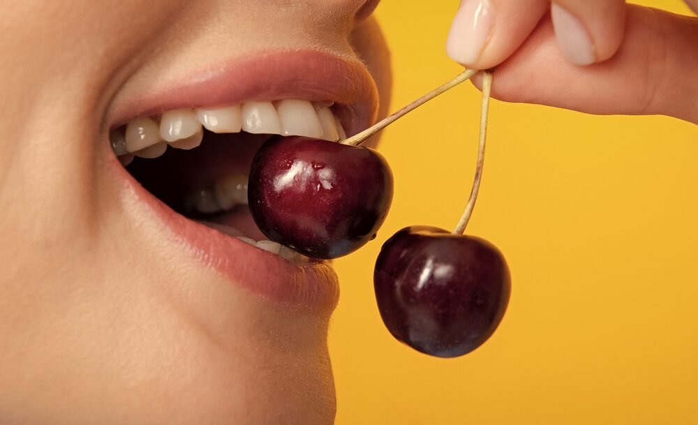 Vibrant cherry biting with healthy teeth against yellow background.