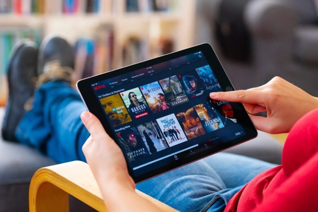 Person browsing Netflix on a tablet with their feet up on a coffee table.