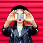 Stylish young adult playfully mimics a kiss with smartphone, vibrant red background.