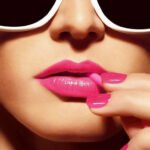 Glamorous woman with pink lipstick and nail polish, wearing white sunglasses.