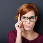 Stylish woman with red hair and green glasses in playful pose.