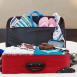 Overpacked red suitcase on bed, chaotic packing for journey.