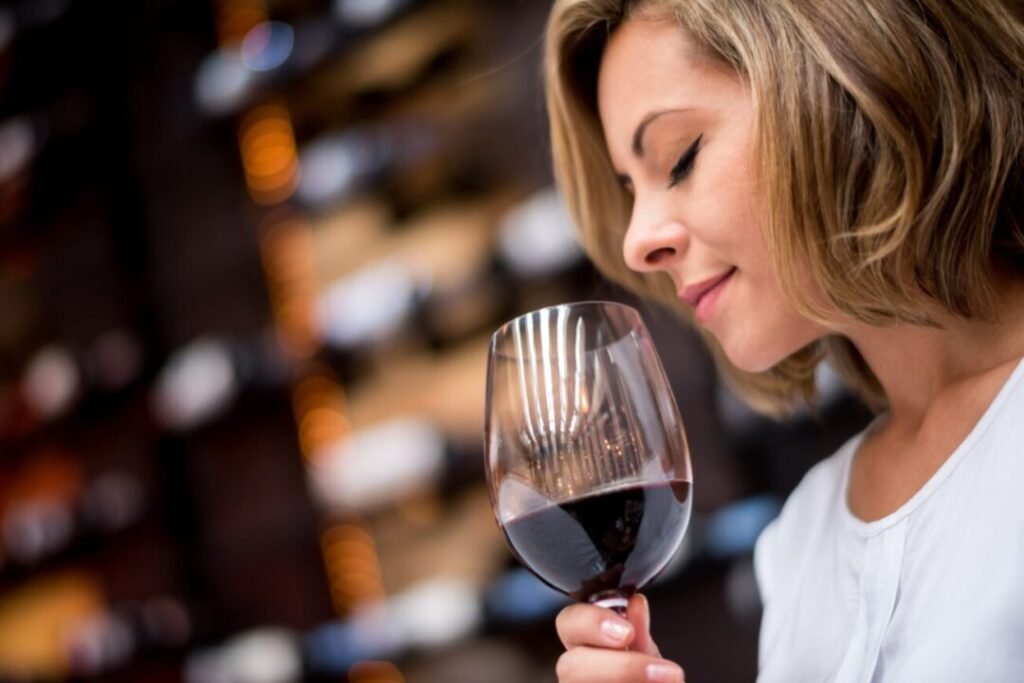 Woman smelling red wine in a large glass with a blurred background of wine shelves.