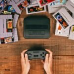 Classic SNES console with colorful game cartridges on wooden surface, hands holding controller.