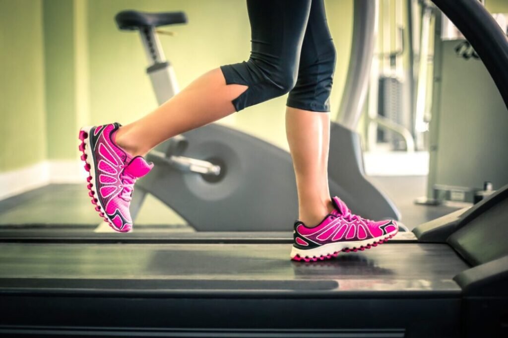 Close-up of a person's legs wearing pink sneakers while running on a treadmill in a gym.